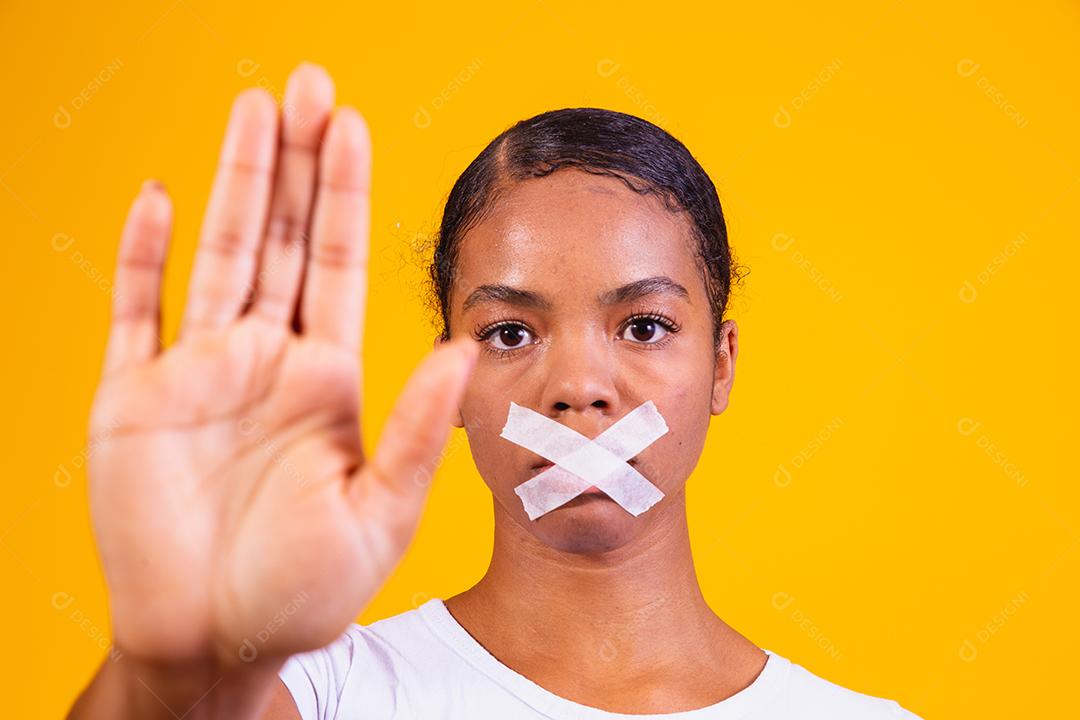 mulher negra em fundo amarelo com a boca fechada em silêncio