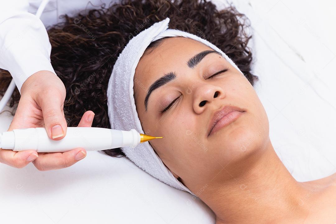 Mulher fazendo tratamento facial com jato de plasma em clínica de beleza.
