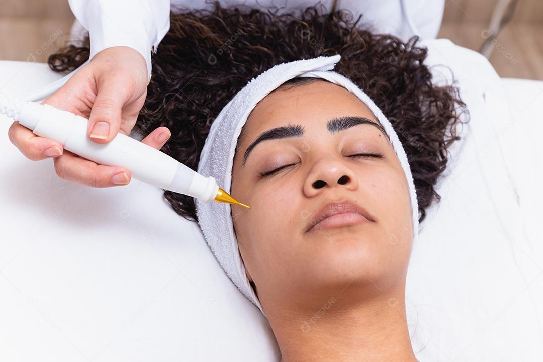 Mulher fazendo tratamento facial com jato de plasma em clínica de beleza.