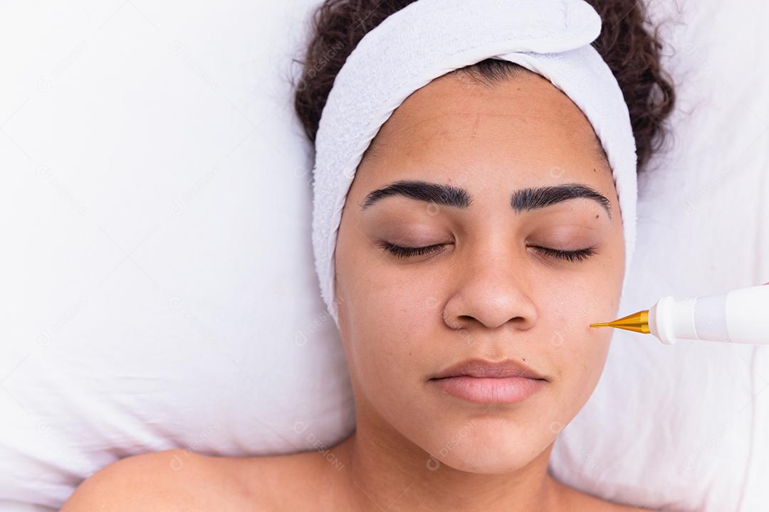Mulher fazendo tratamento facial com jato de plasma em clínica de beleza.