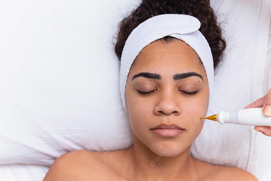 Mulher fazendo tratamento facial com jato de plasma em clínica de beleza.