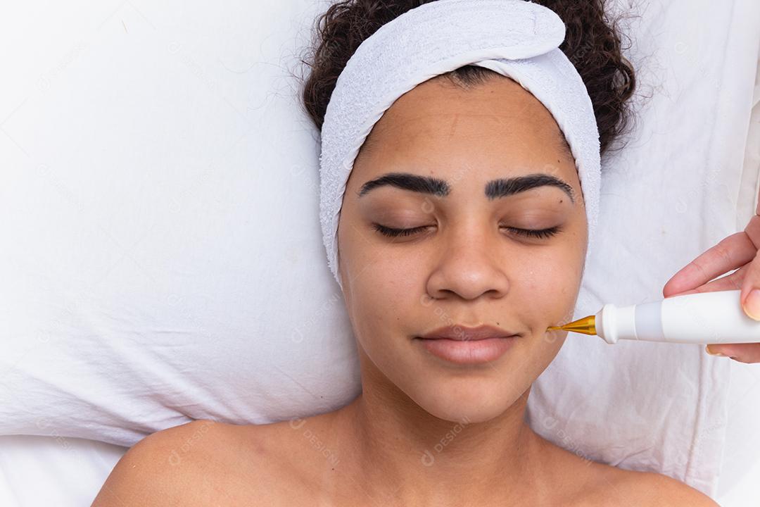 Mulher fazendo tratamento facial com jato de plasma em clínica de beleza.