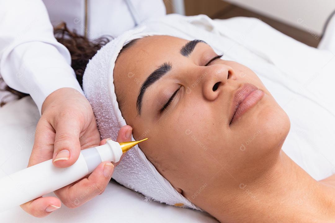 Mulher fazendo tratamento facial com jato de plasma em clínica de beleza.