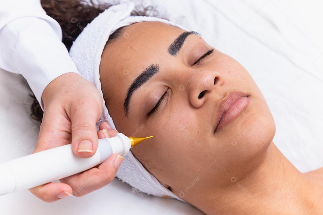 Mulher fazendo tratamento facial com jato de plasma em clínica de beleza.