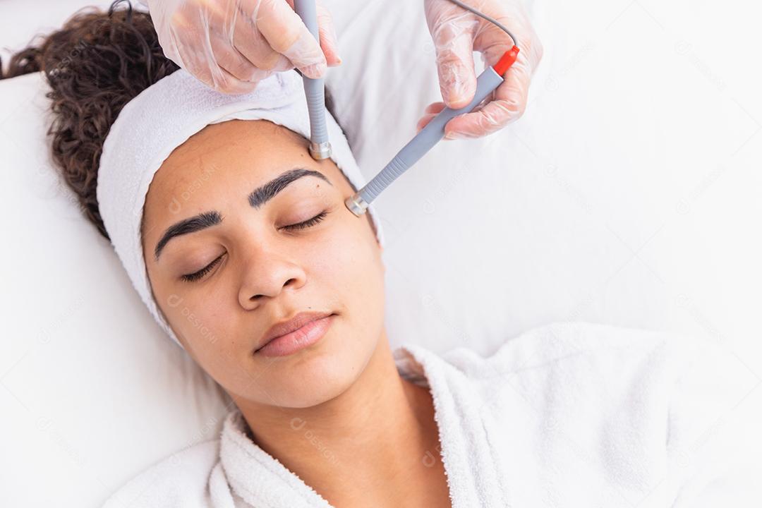 Jovem deitada na mesa do cosmetologista durante o procedimento de rejuvenescimento. Cosmetologista cuida da pele do pescoço