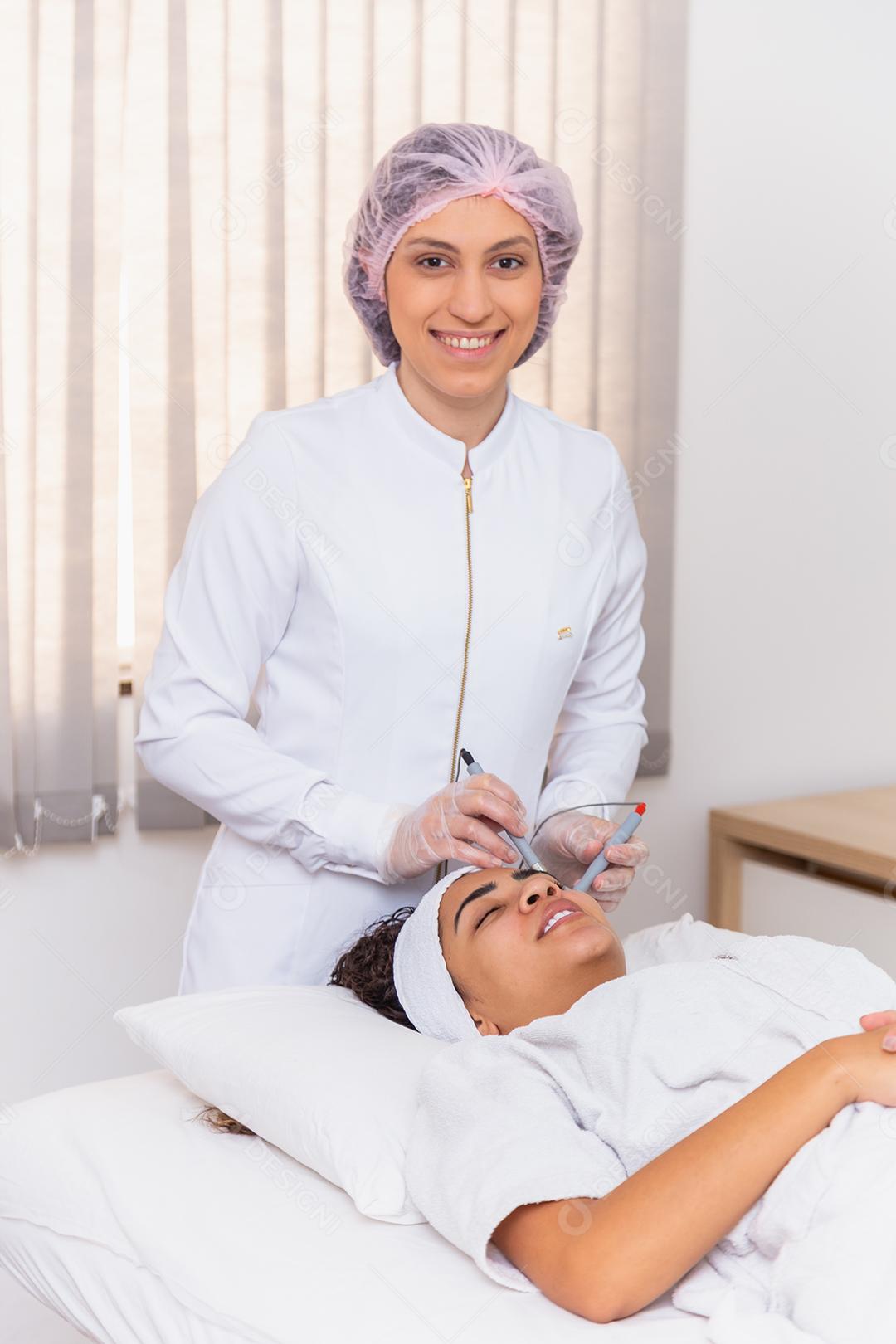 Jovem deitada na mesa do cosmetologista durante o procedimento de rejuvenescimento. Cosmetologista cuida da pele do pescoço