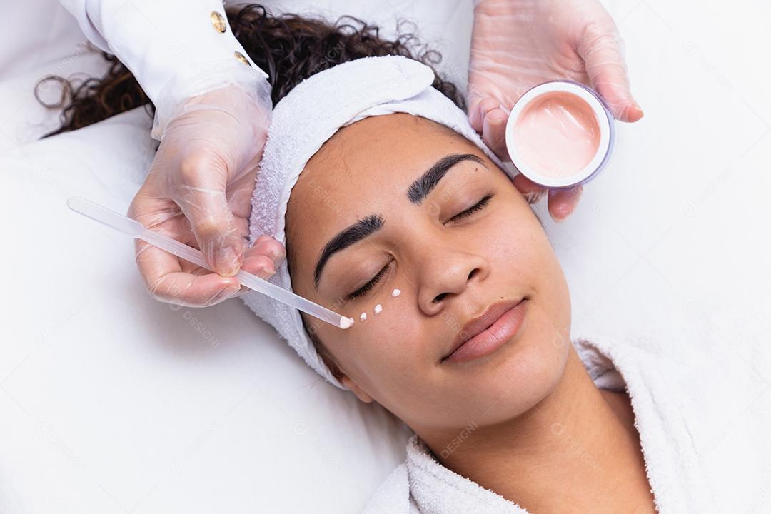 Mulher bonita com gotas de creme no rosto e o frasco ao lado. Mulher aplicando creme para o rosto. conceito de spa