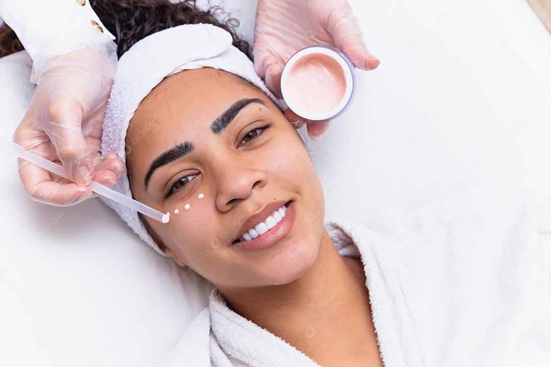 Mulher bonita com gotas de creme no rosto e o frasco ao lado. Mulher aplicando creme para o rosto. conceito de spa