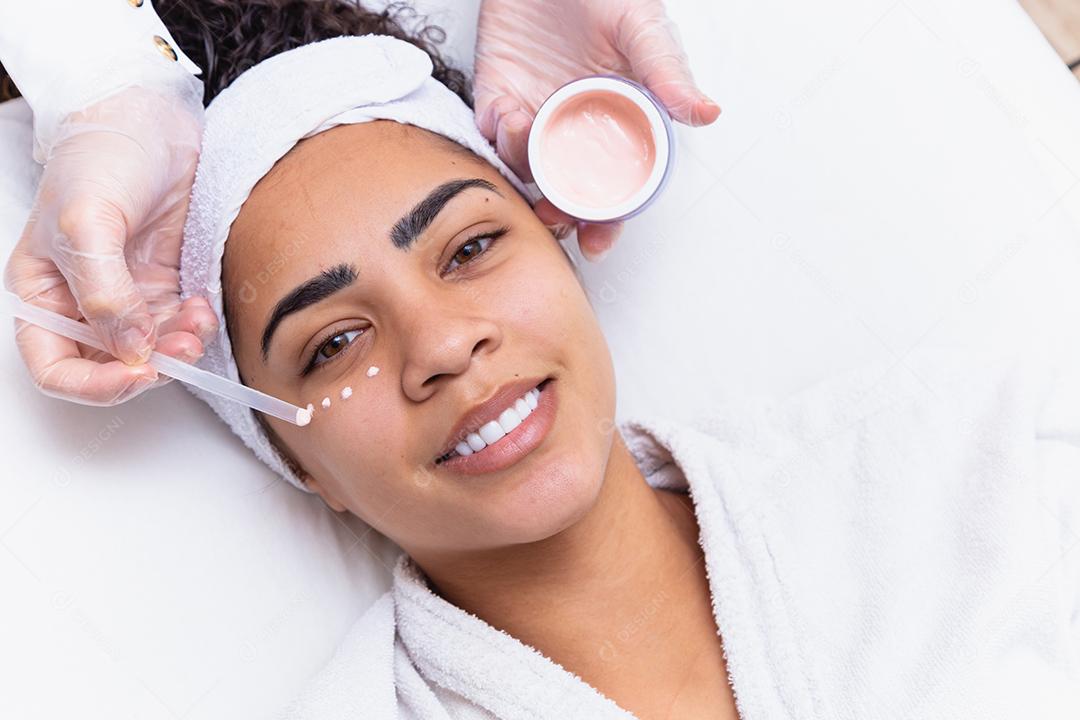 Mulher bonita com gotas de creme no rosto e o frasco ao lado. Mulher aplicando creme para o rosto. conceito de spa