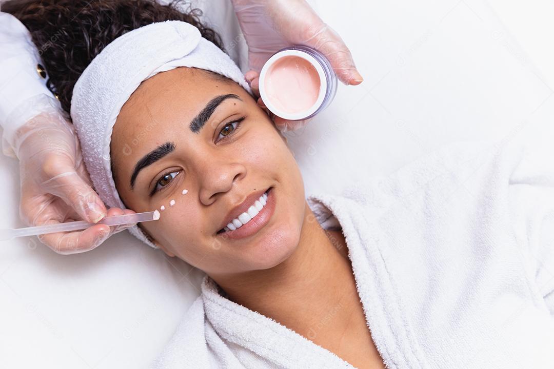 Mulher bonita com gotas de creme no rosto e o frasco ao lado. Mulher aplicando creme para o rosto. conceito de spa