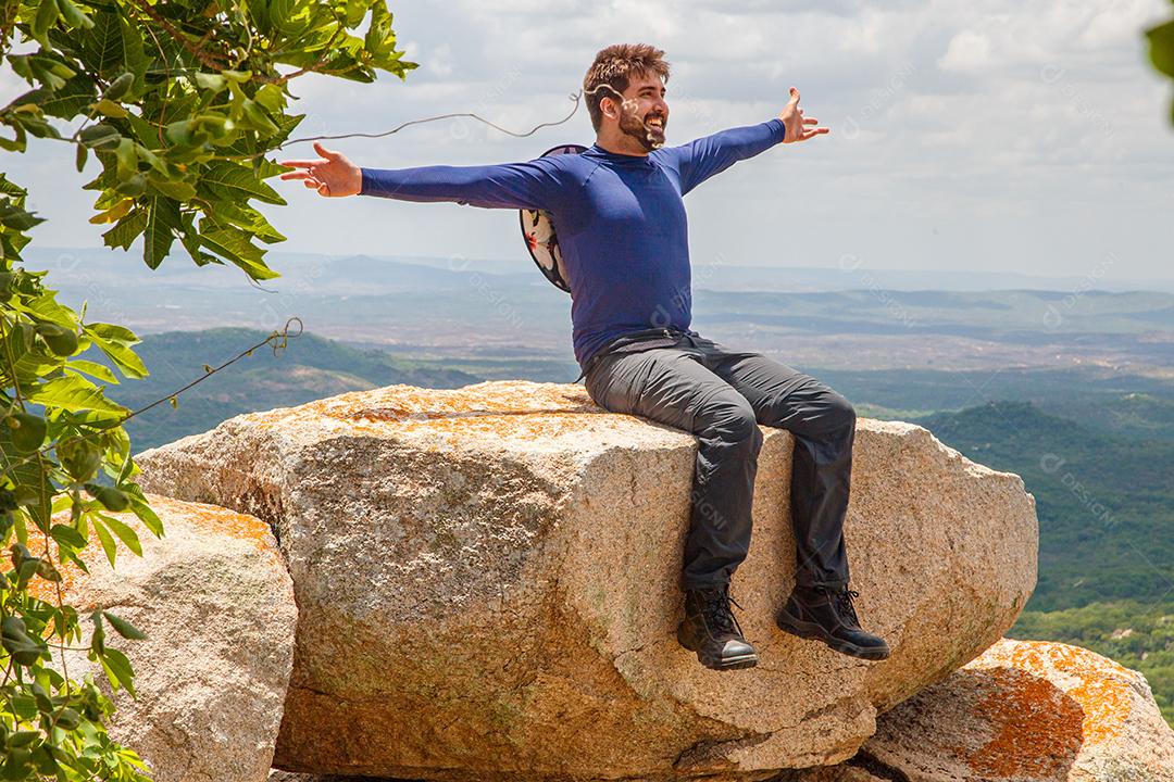homem de braços abertos, sentado na rocha em uma montanha. Conceito de aventura e vitória