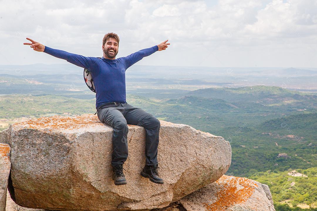 man with open arms sitting on rock in a mountain. Concept of adventure and victory