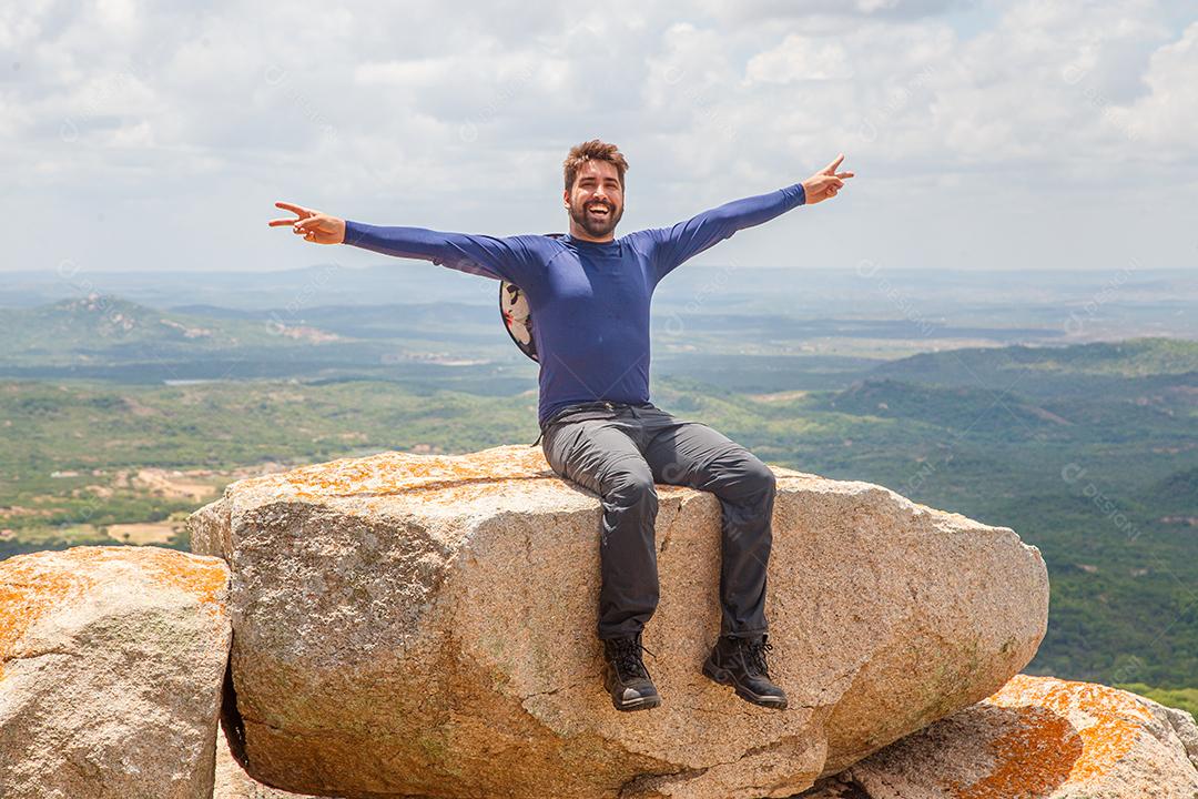 homem de braços abertos, sentado na rocha em uma montanha. Conceito de aventura e vitória