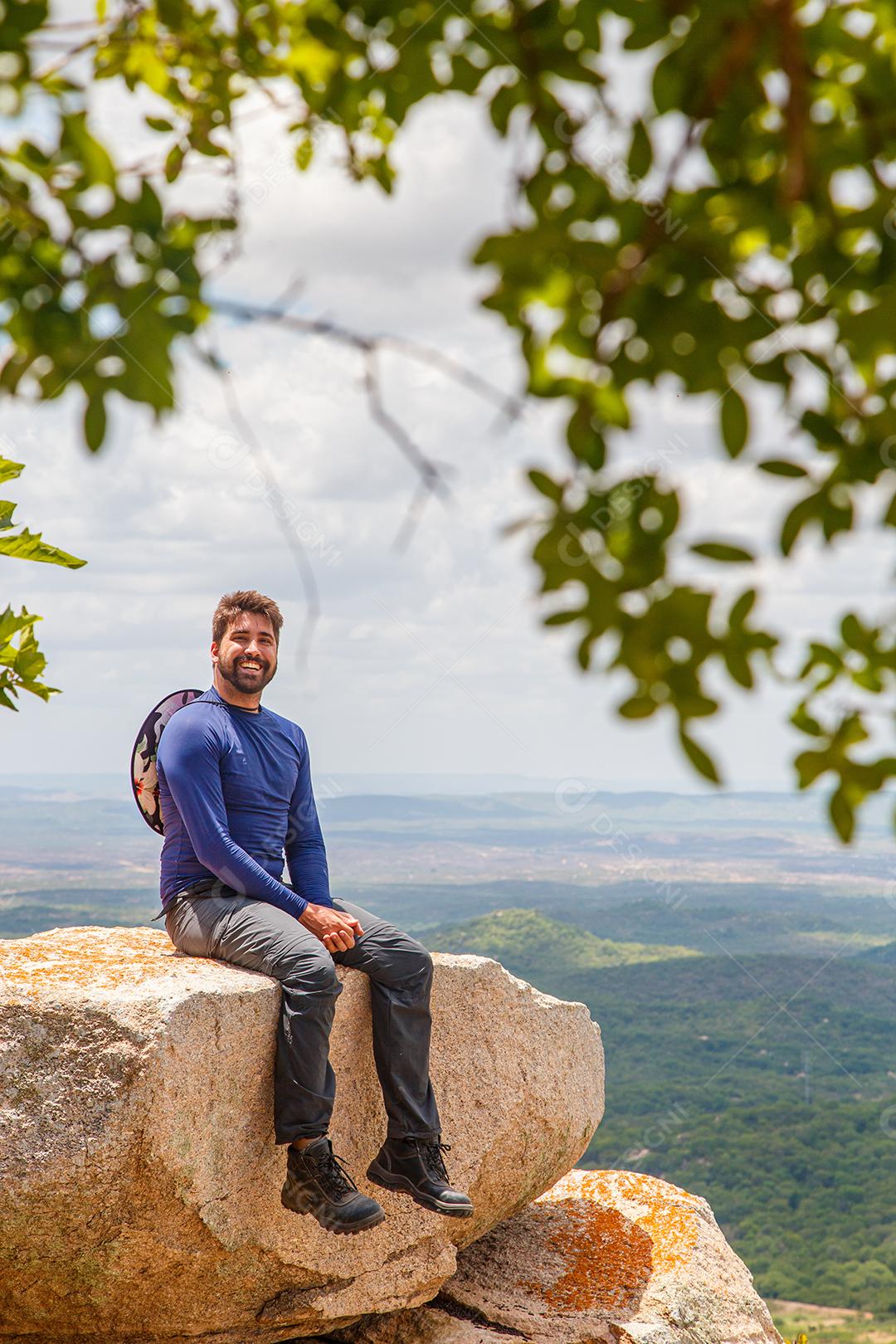 homem de braços abertos, sentado na rocha em uma montanha. Conceito de aventura e vitória