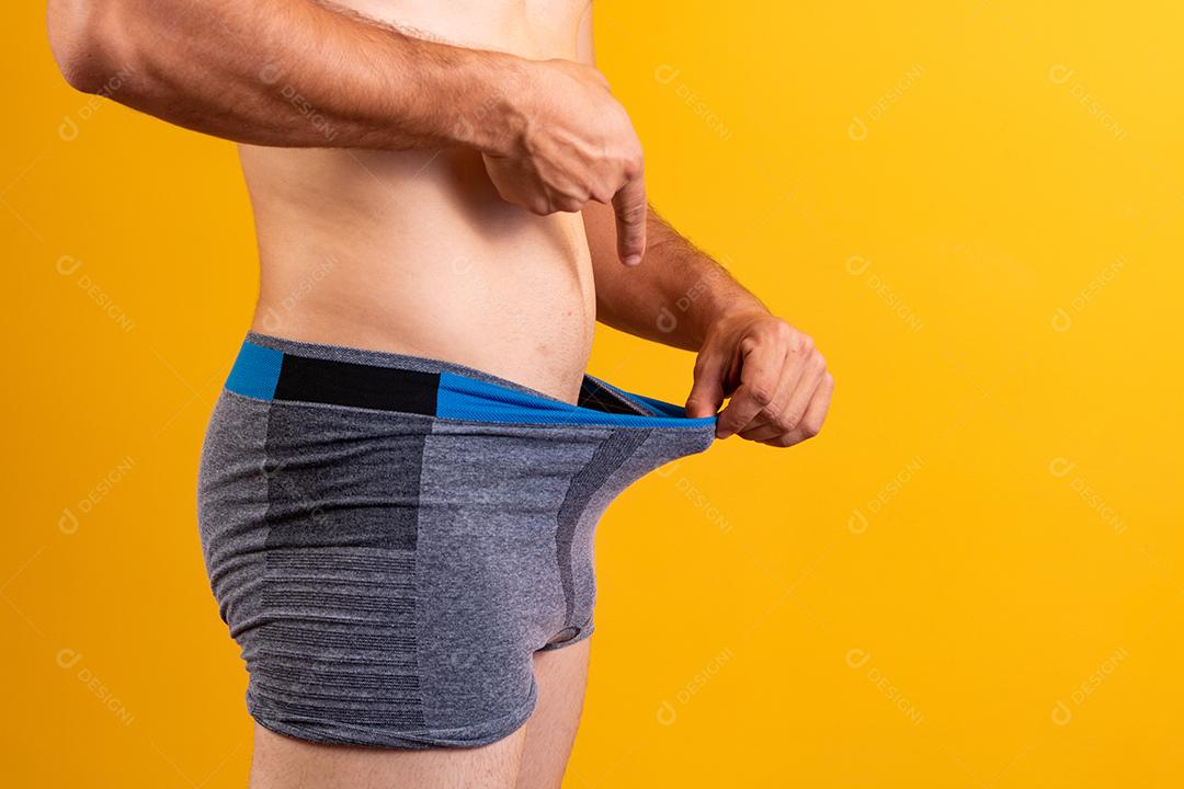 Desportivo jovem adulto puxa cueca boxer cinza escuro e apontando seus genitais,