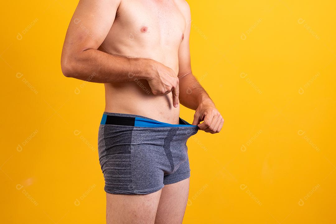 Desportivo jovem adulto puxa cueca boxer cinza escuro e apontando seus genitais,