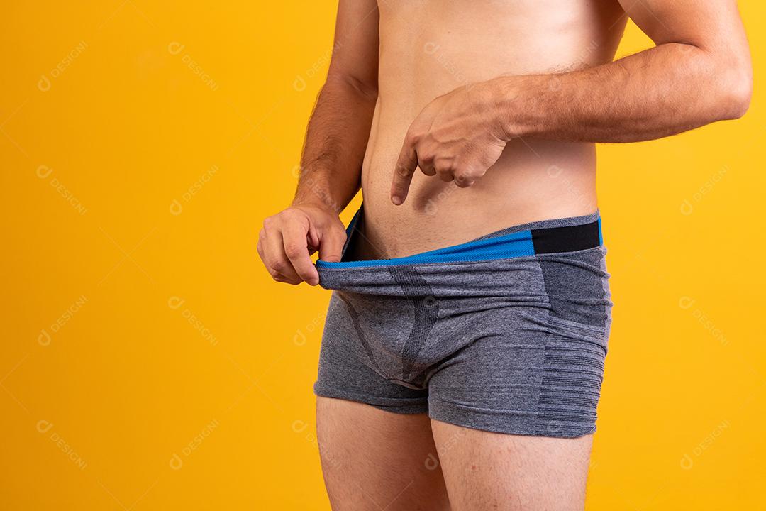 Desportivo jovem adulto puxa cueca boxer cinza escuro e apontando seus genitais,