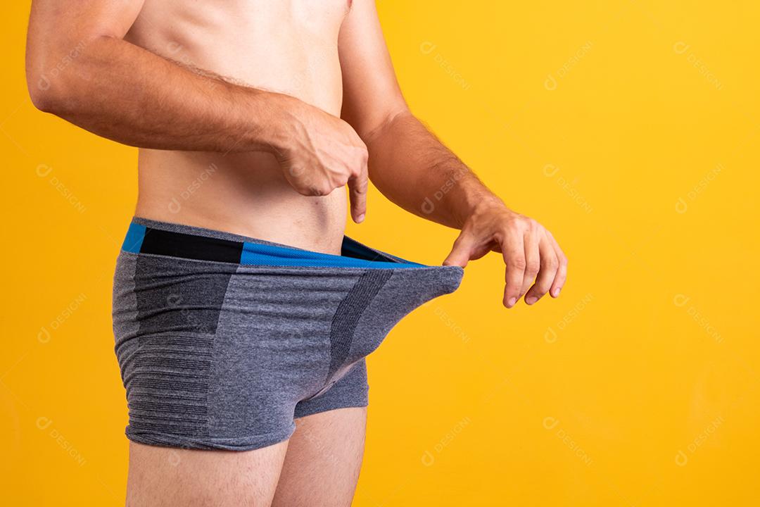 Desportivo jovem adulto puxa cueca boxer cinza escuro e apontando seus genitais,