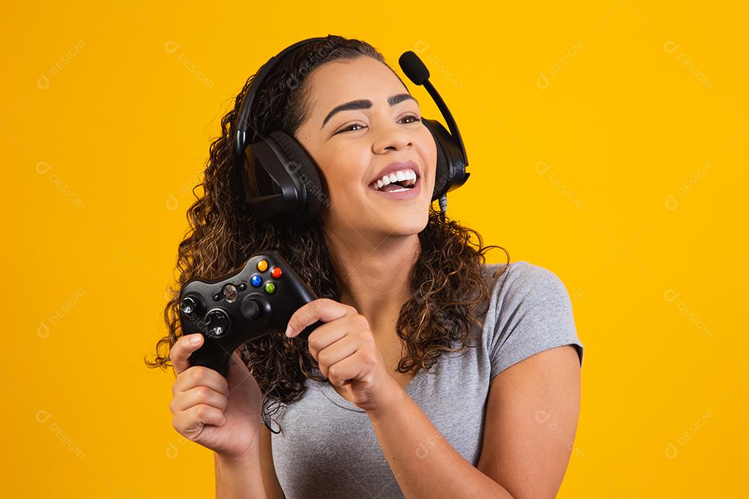 Mulher excitada jogando videogame em fundo amarelo.