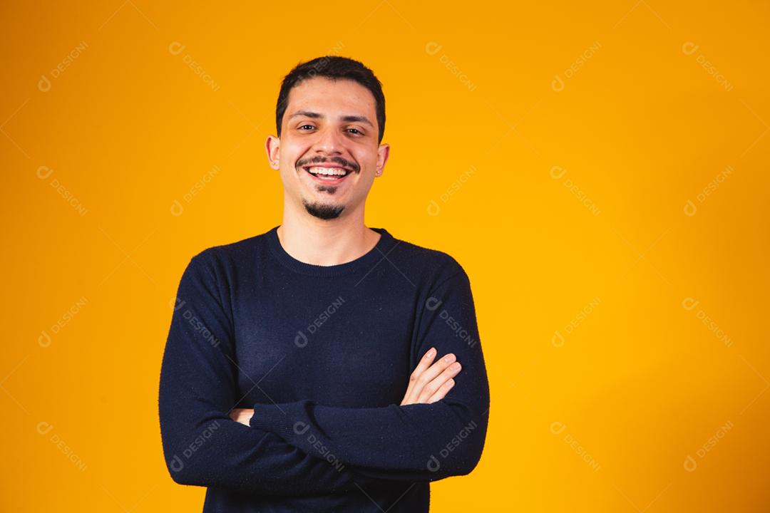 Rapaz com os braços cruzados sorrindo em fundo amarelo