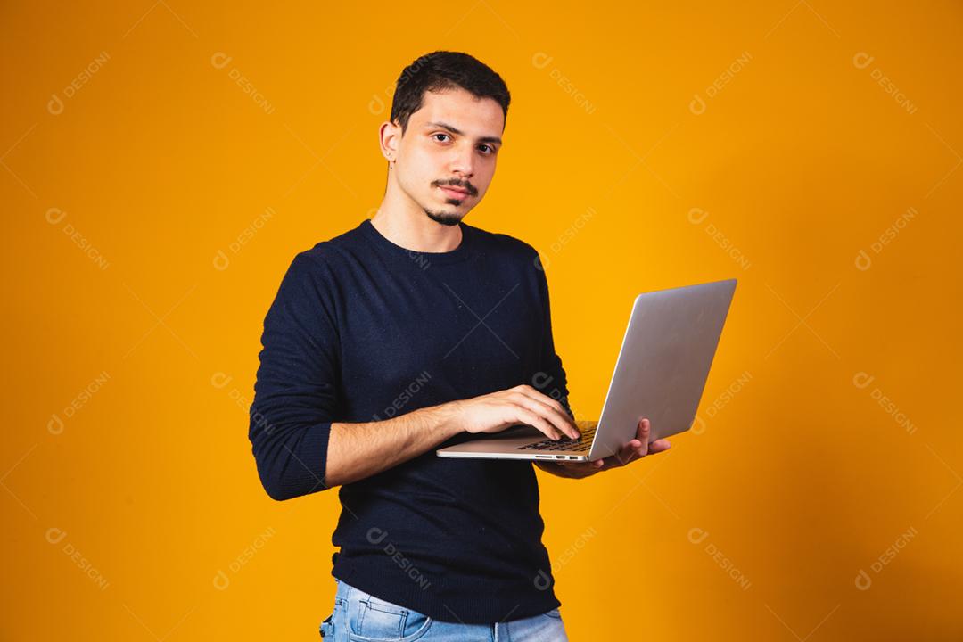 Retrato de menino segurando laptop trabalhando nas mãos em fundo amarelo