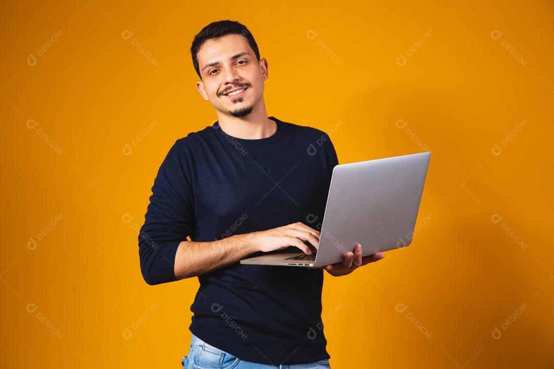 Retrato de menino segurando laptop trabalhando nas mãos em fundo amarelo