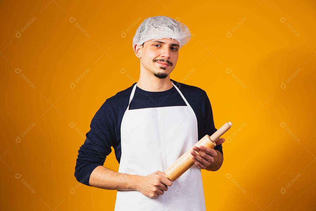 Fabricante de pizza de menino em fundo amarelo, segurando o rolo.