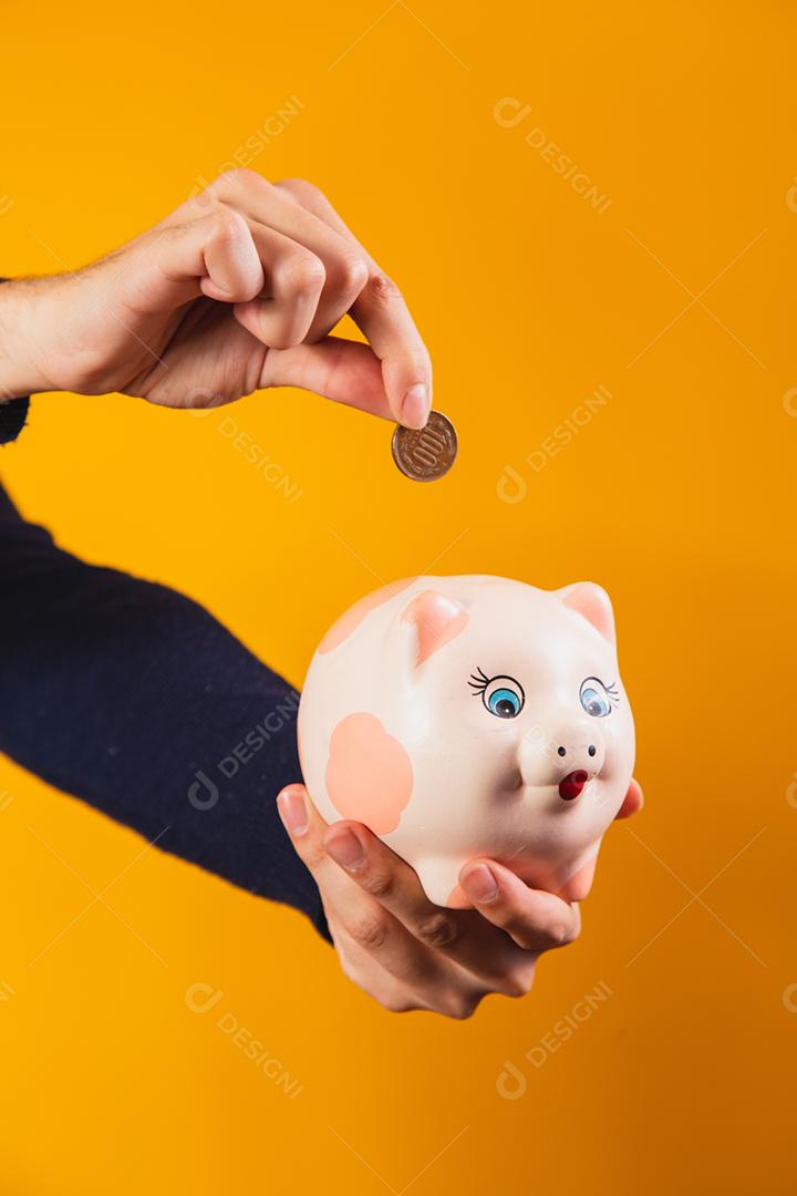 Closeup na mão depositando moedas no cofrinho.