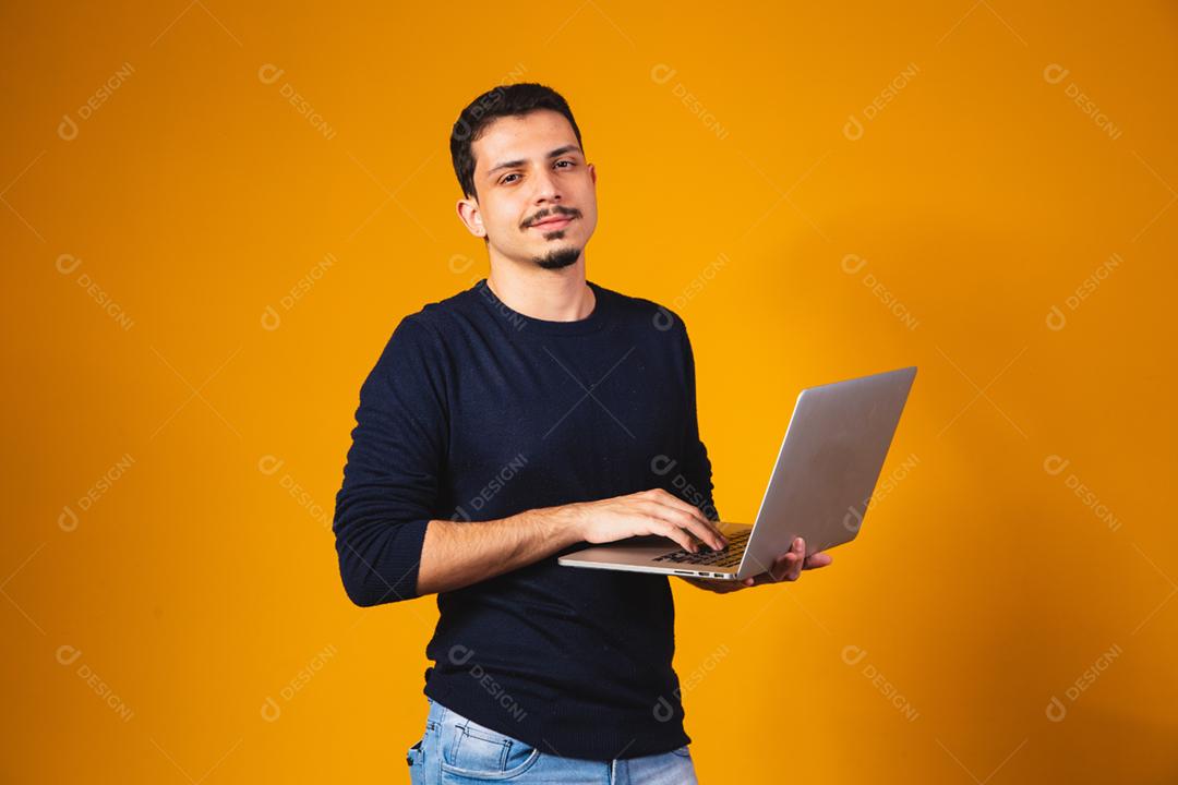 Retrato de menino segurando laptop trabalhando nas mãos em fundo amarelo