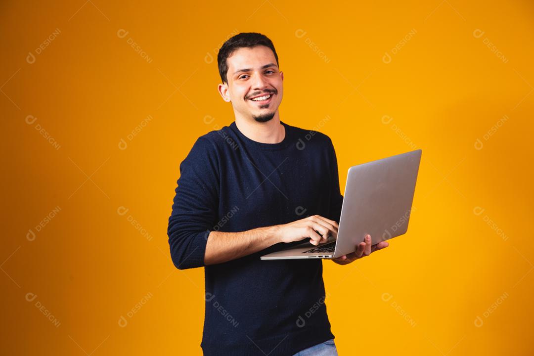 Retrato de menino segurando laptop trabalhando nas mãos em fundo amarelo