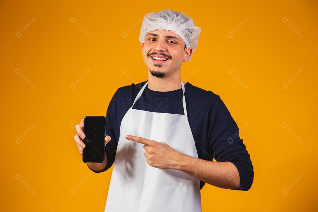 Menino de avental apontando para celular. Estudante de gastronomia em amarelo