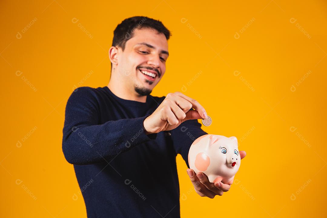 Empresário economizando dinheiro colocando moedas no cofrinho. jovem b