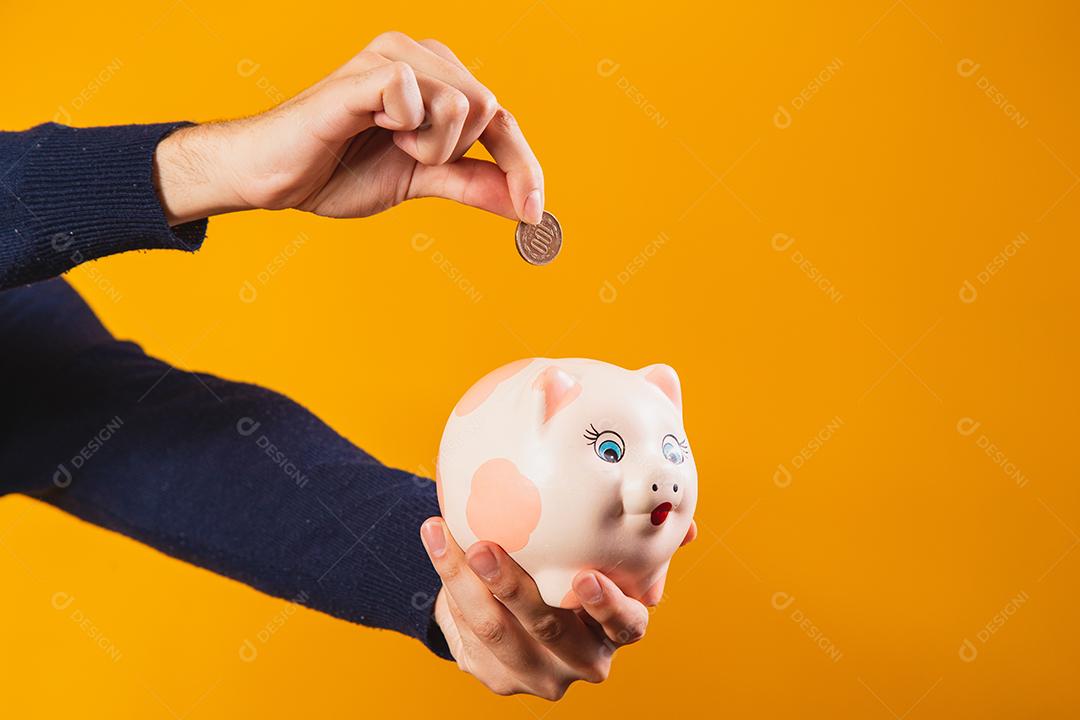 Closeup na mão depositando moedas no cofrinho.