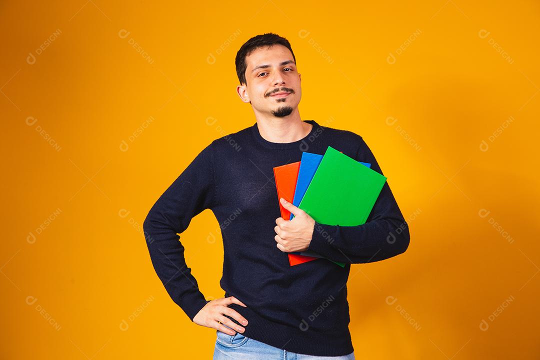Menino jovem estudante sobre fundo amarelo. menino estudante feliz segurando