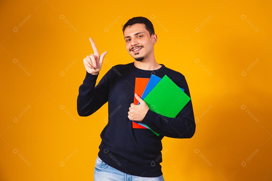 Menino jovem estudante sobre fundo amarelo. menino estudante feliz segurando