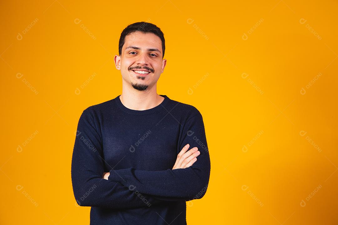 Menino com os braços cruzados sorrindo em fundo amarelo