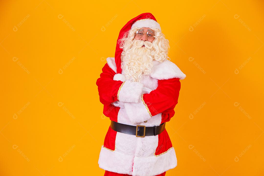 Papai Noel com os braços cruzados sobre fundo amarelo.