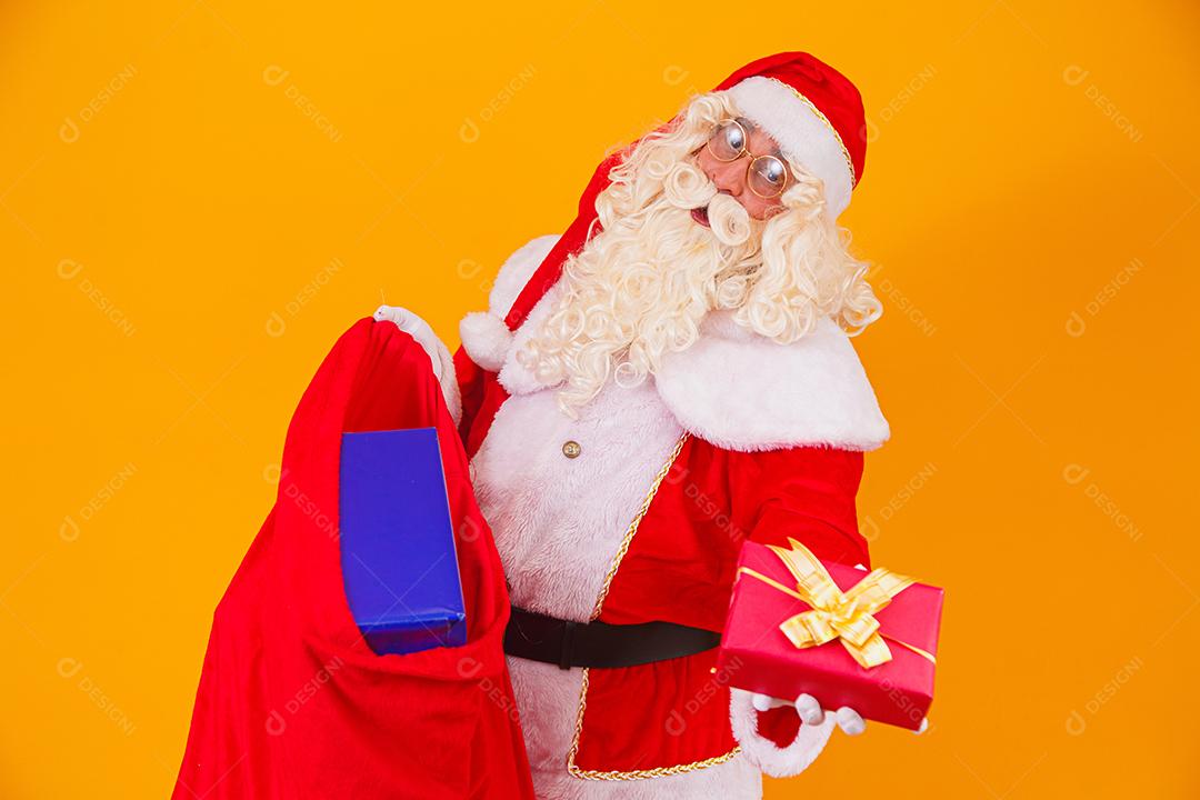 Real Santa Claus on yellow background holding bag with various c