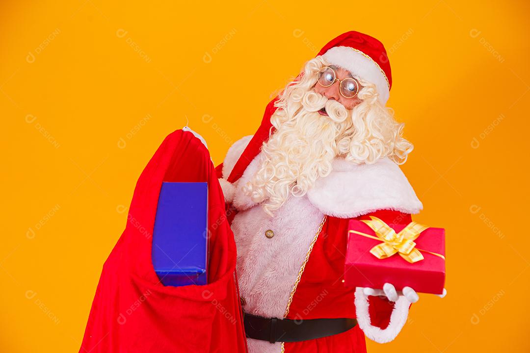 Verdadeiro Papai Noel em fundo amarelo segurando saco com vários c