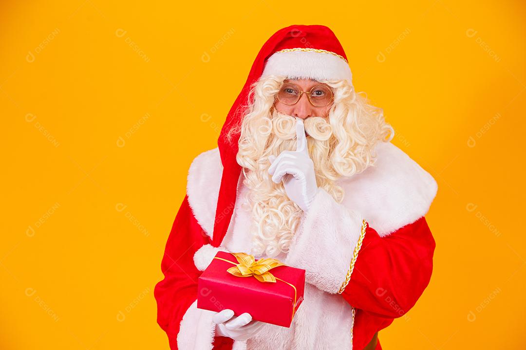 Papai Noel em fundo amarelo segurando um presente nas mãos e mak