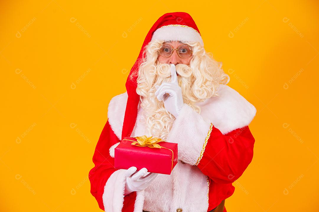 Papai Noel em fundo amarelo segurando um presente nas mãos e mak