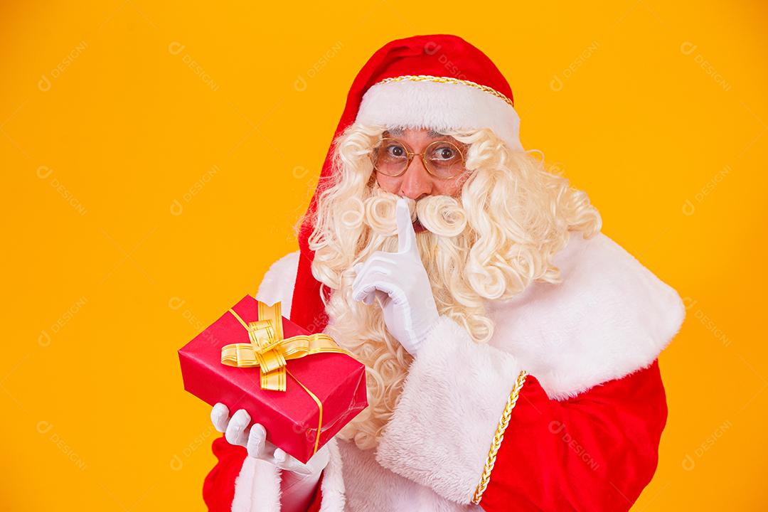 Papai Noel em fundo amarelo segurando um presente nas mãos e mak