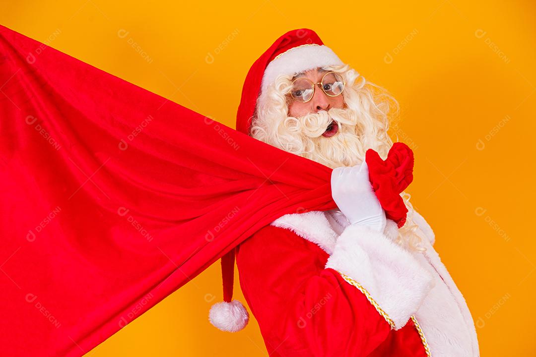 Papai Noel em fundo amarelo, segurando o saco com presentes nas costas. Papai Noel fazendo uma surpresa na noite de Natal