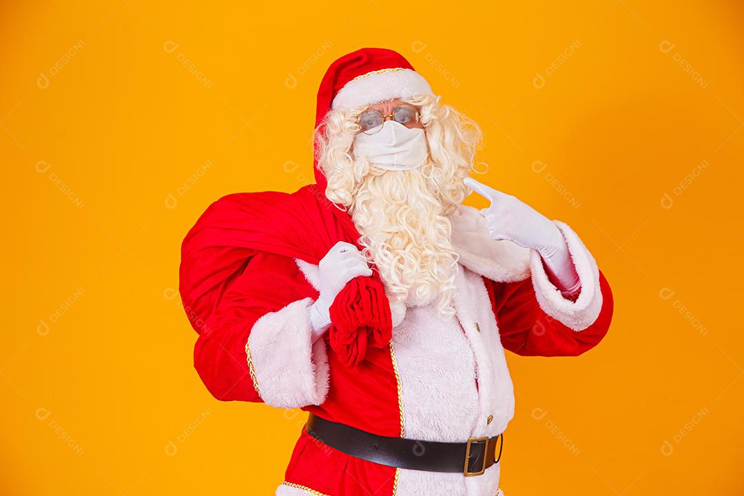 Real Papai Noel em fundo amarelo, usando máscara protetora contra o covid19. Natal com distanciamento social. Covid-19