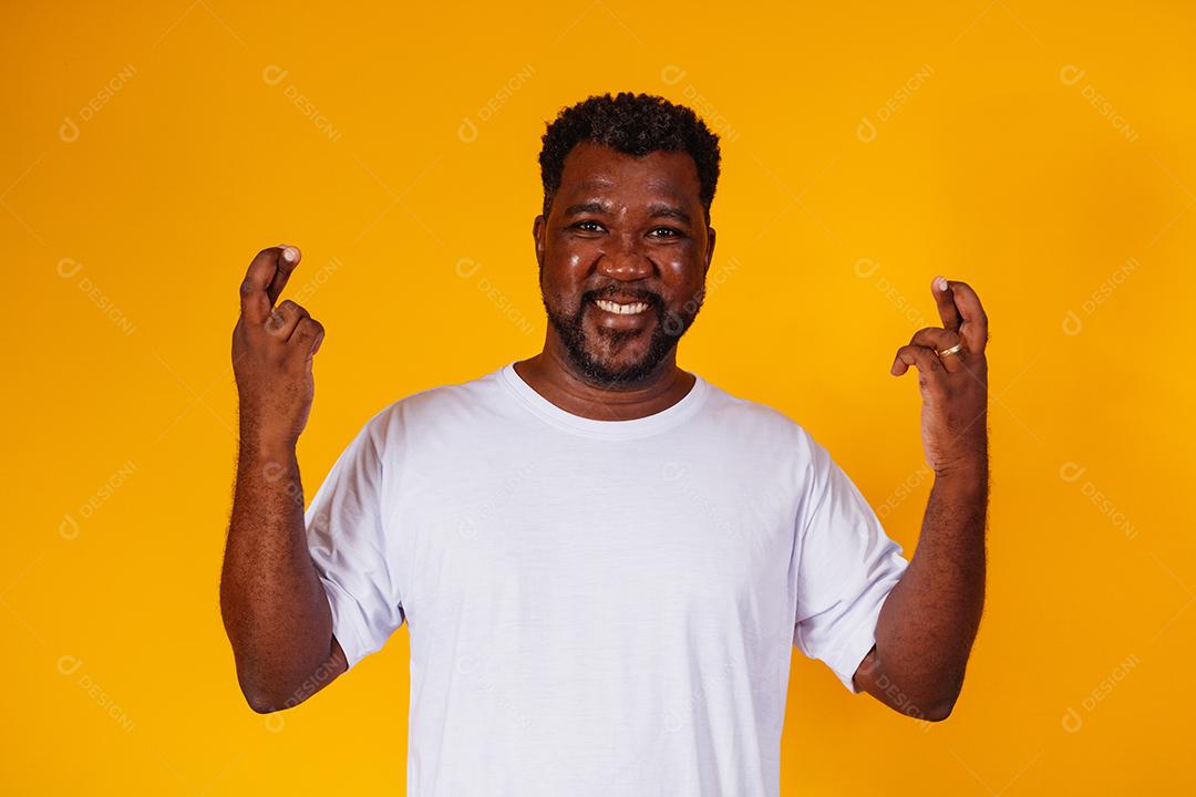 homem afro com os dedos cruzados no fundo amarelo