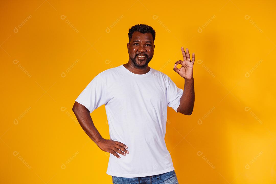 Retrato de homem afro-americano feliz mostrando sinal de ok e sorrindo, sobre fundo amarelo.