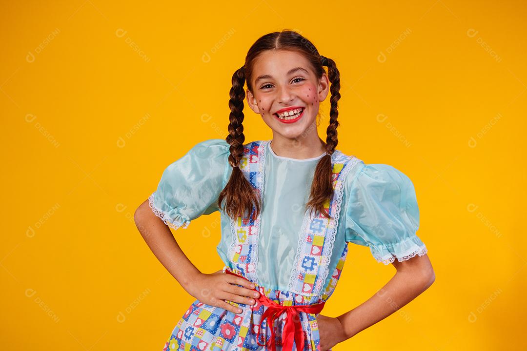 Criança com roupas típicas da famosa festa brasileira chamada Festa Junina em comemoração ao São João. Linda garota em fundo amarelo.