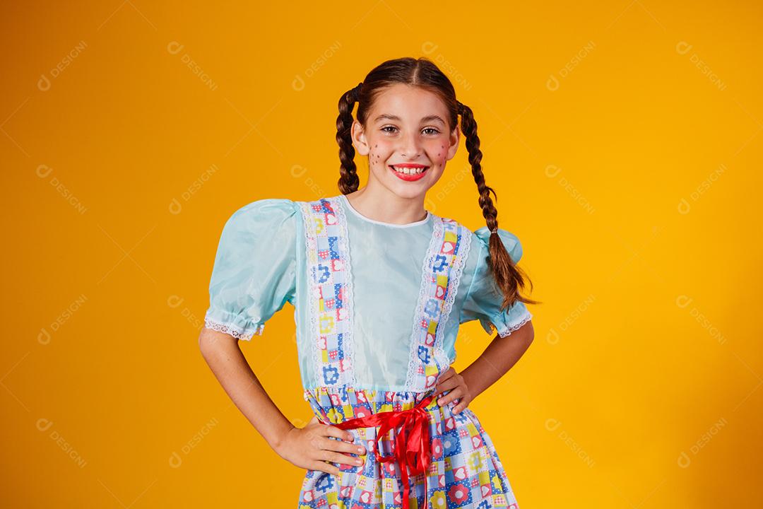 Criança com roupas típicas da famosa festa brasileira chamada Festa Junina em comemoração ao São João. Linda garota em fundo amarelo.