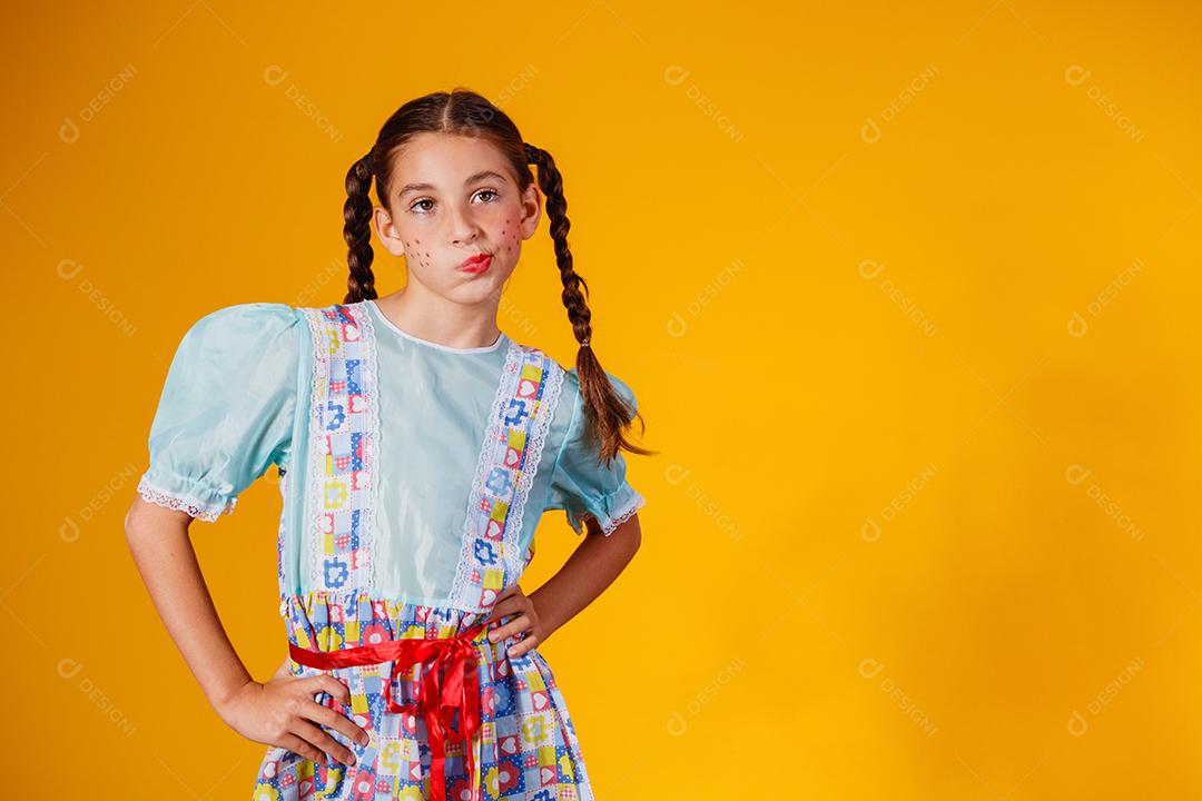 Criança com roupas típicas da famosa festa brasileira chamada Festa Junina em comemoração ao São João. Linda garota em fundo amarelo.