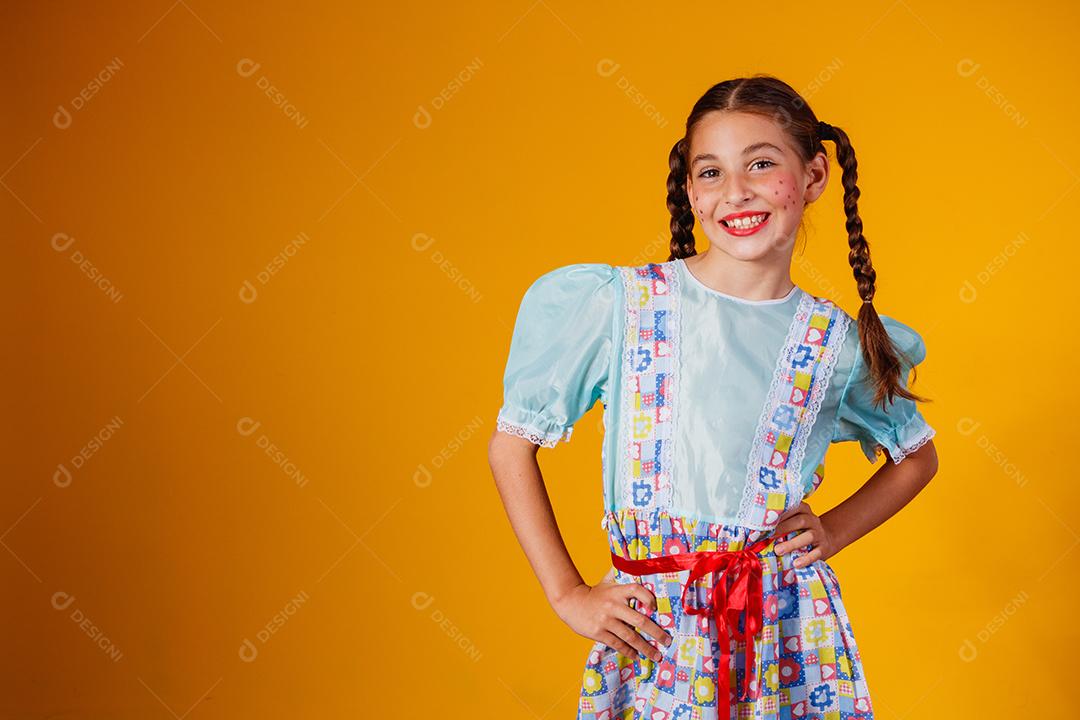 Criança com roupas típicas da famosa festa brasileira chamada Festa Junina em comemoração ao São João. Linda garota em fundo amarelo.